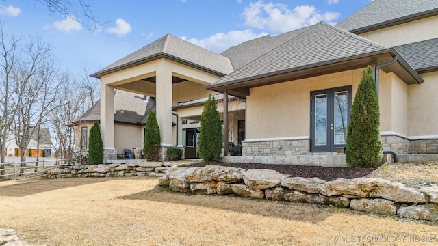 back of house with fence, french doors, stone siding, and roof with shingles