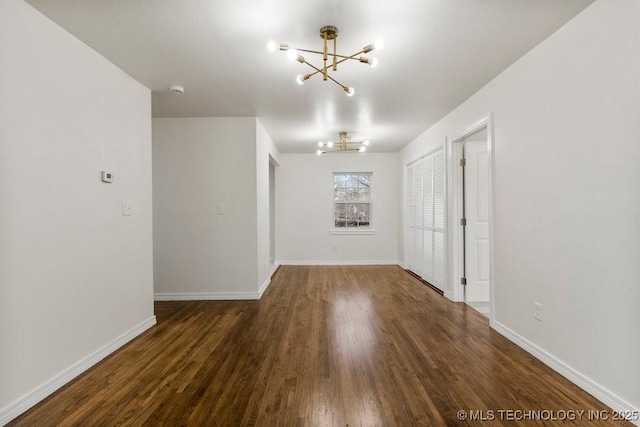 spare room featuring an inviting chandelier, wood finished floors, and baseboards