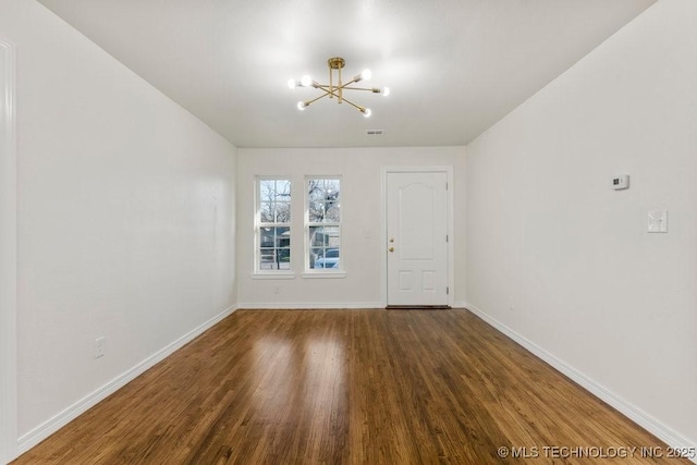 spare room featuring visible vents, baseboards, a notable chandelier, and wood finished floors