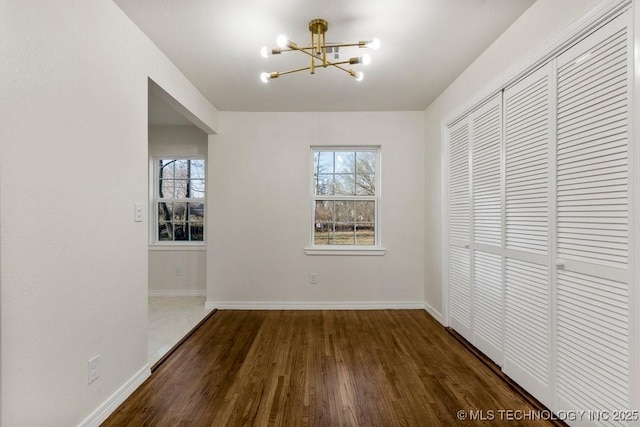 unfurnished dining area featuring baseboards, an inviting chandelier, and wood finished floors