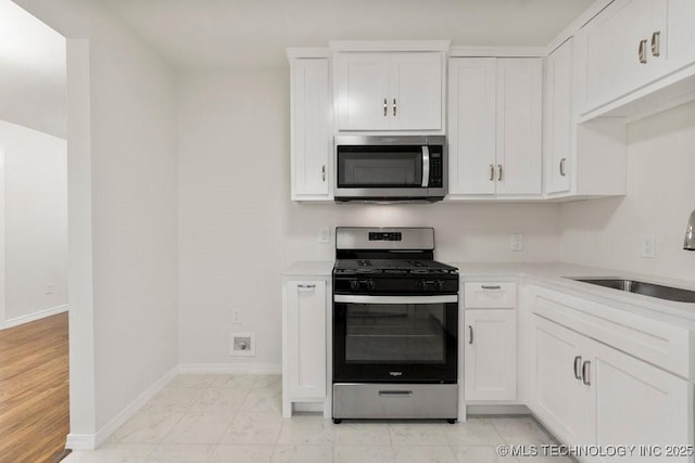 kitchen with a sink, stainless steel appliances, light countertops, white cabinetry, and marble finish floor