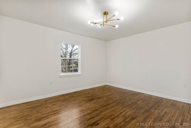 empty room featuring a notable chandelier, wood finished floors, and baseboards