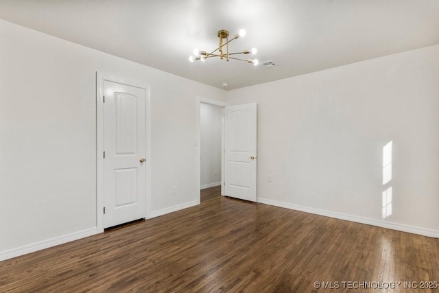 spare room featuring visible vents, baseboards, an inviting chandelier, and wood finished floors