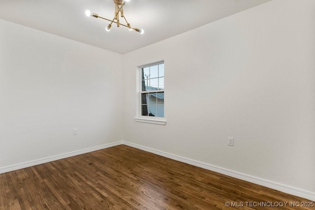 spare room with dark wood finished floors, an inviting chandelier, and baseboards