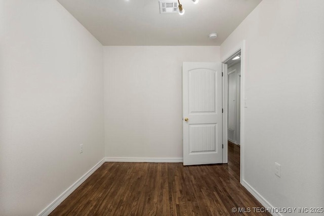 empty room featuring visible vents, baseboards, and dark wood finished floors