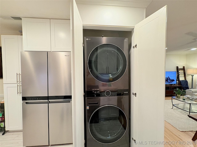 clothes washing area featuring visible vents, light wood-style flooring, and stacked washer / drying machine