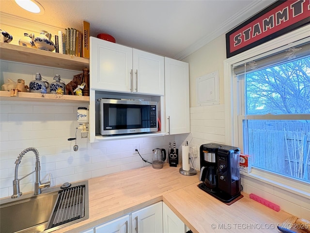 kitchen featuring open shelves, a sink, crown molding, white cabinetry, and stainless steel microwave