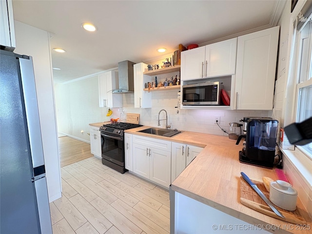 kitchen with appliances with stainless steel finishes, light countertops, wall chimney range hood, and a sink