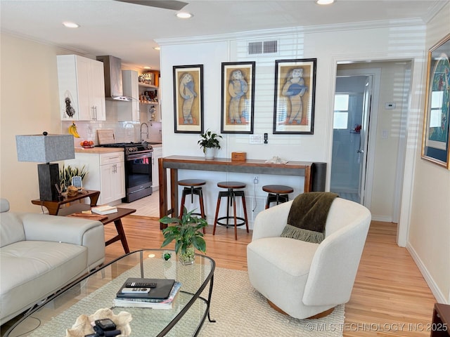 living room with visible vents, crown molding, baseboards, recessed lighting, and light wood-style floors