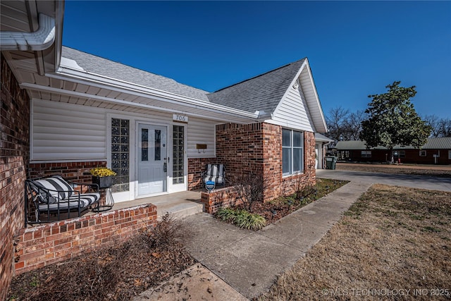 view of exterior entry with brick siding, concrete driveway, an attached garage, and a shingled roof