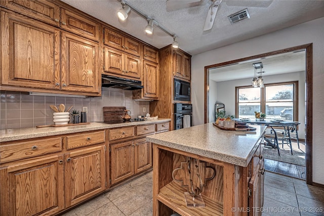 kitchen featuring under cabinet range hood, brown cabinets, backsplash, and black appliances