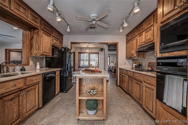 kitchen featuring backsplash, under cabinet range hood, brown cabinets, black appliances, and a sink