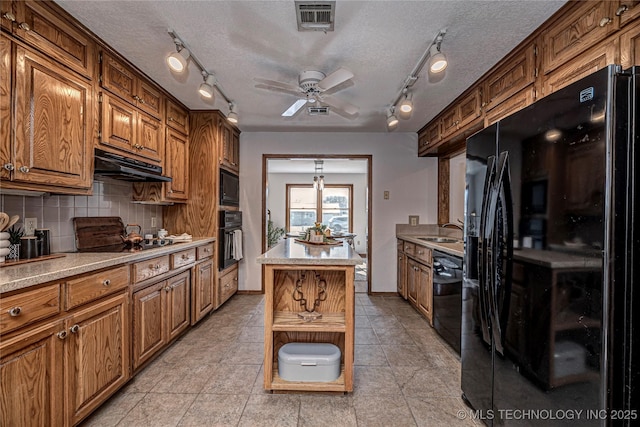 kitchen with visible vents, black appliances, under cabinet range hood, a sink, and decorative backsplash