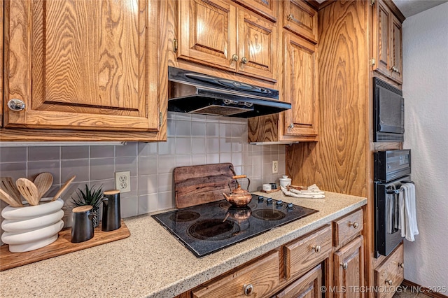 kitchen with under cabinet range hood, backsplash, black appliances, and brown cabinetry