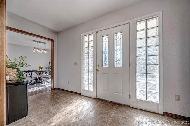 tiled entryway with baseboards, a notable chandelier, and a textured ceiling