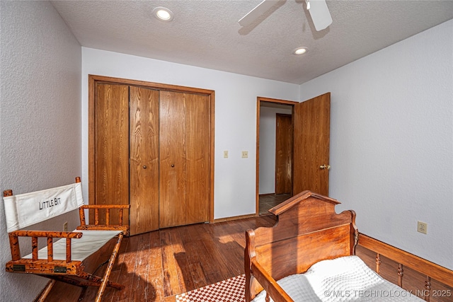 bedroom with baseboards, hardwood / wood-style flooring, a closet, a textured ceiling, and a textured wall