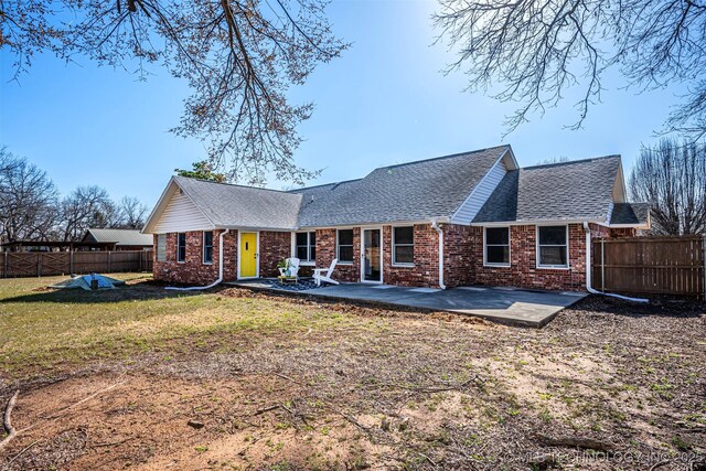 rear view of house with brick siding, a shingled roof, fence, a yard, and a patio