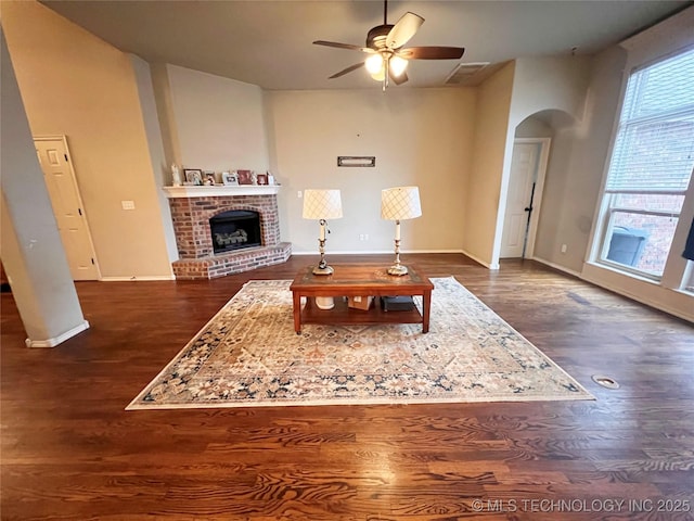 living room with arched walkways, visible vents, a brick fireplace, and dark wood-style flooring