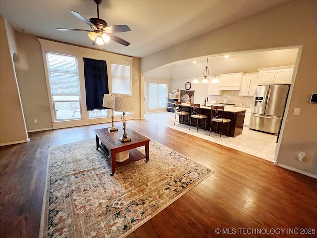 living room with light wood-type flooring, lofted ceiling, baseboards, and ceiling fan with notable chandelier