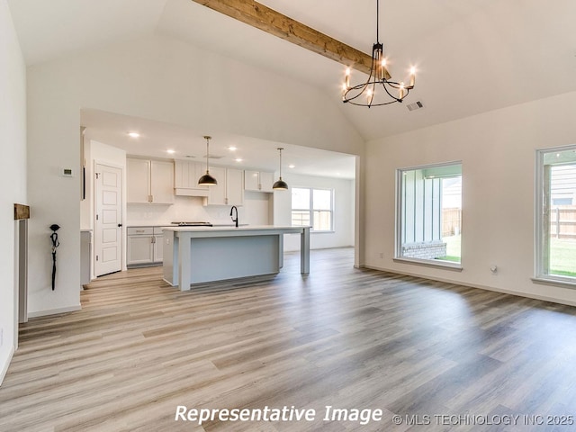 kitchen featuring visible vents, open floor plan, light wood-type flooring, a notable chandelier, and a kitchen island with sink