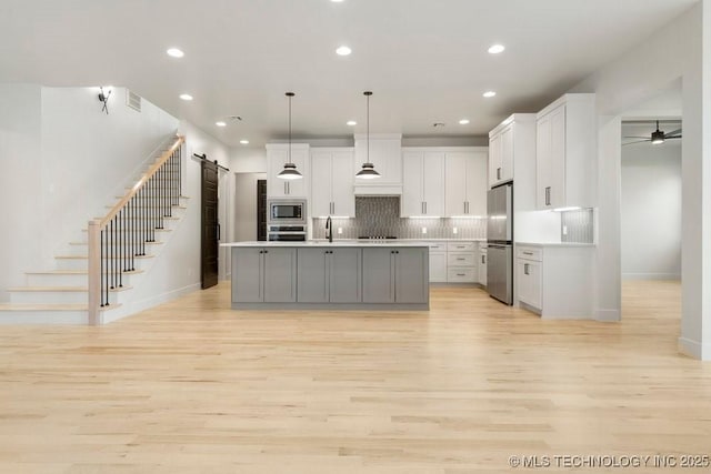 kitchen featuring light wood finished floors, tasteful backsplash, a barn door, appliances with stainless steel finishes, and white cabinetry