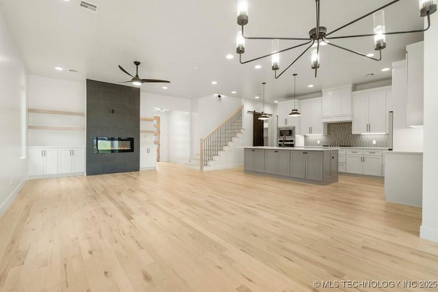 kitchen with custom exhaust hood, open floor plan, a tiled fireplace, and light wood finished floors