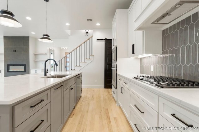 kitchen with ventilation hood, a barn door, decorative backsplash, stainless steel appliances, and a sink