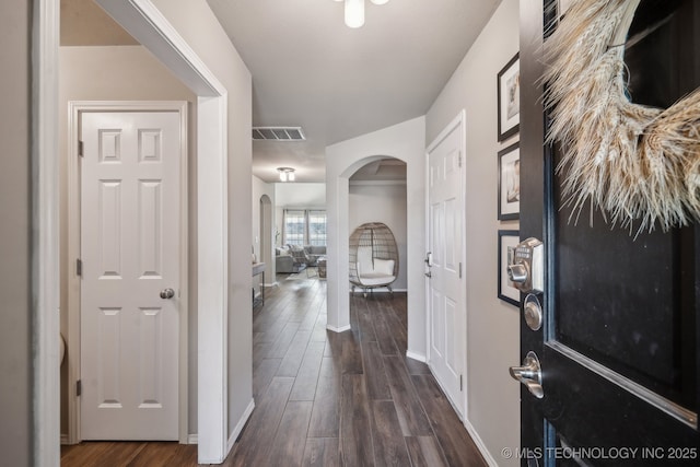 entryway featuring dark wood-type flooring, arched walkways, visible vents, and baseboards