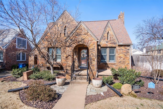 tudor house featuring stone siding, a high end roof, and fence