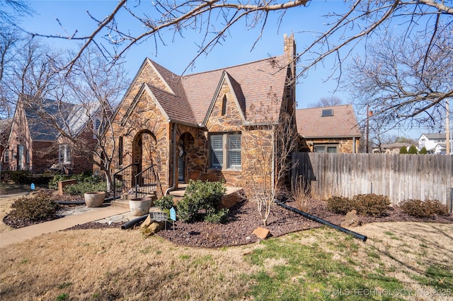 tudor home with a front lawn, fence, stone siding, and a chimney