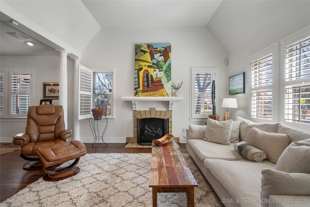 living room with a fireplace with flush hearth, wood finished floors, baseboards, decorative columns, and lofted ceiling