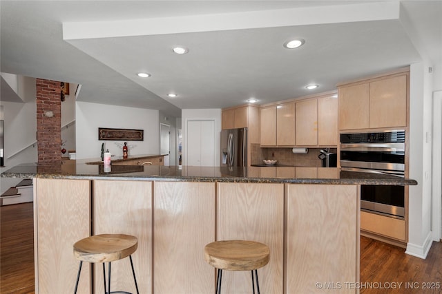 kitchen with a kitchen breakfast bar, dark wood-type flooring, appliances with stainless steel finishes, and light brown cabinetry