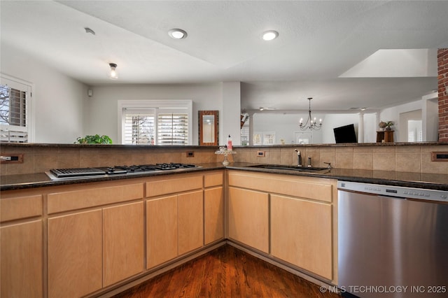 kitchen with a sink, gas cooktop, stainless steel dishwasher, tasteful backsplash, and a chandelier