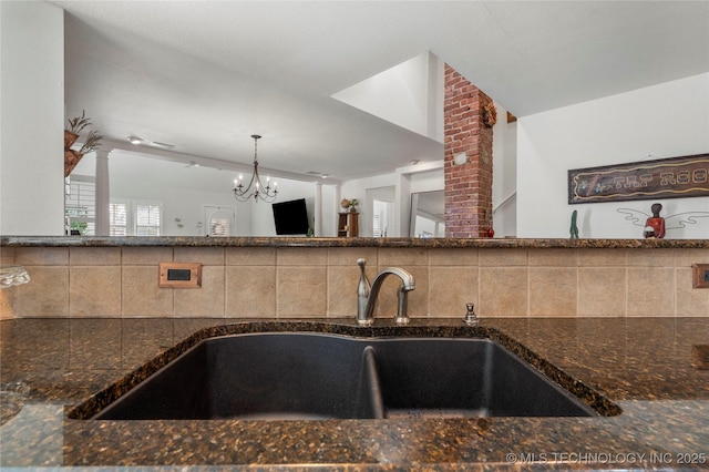 kitchen featuring dark stone counters, decorative light fixtures, backsplash, and a sink