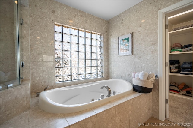 bathroom with tile walls, a jetted tub, a spacious closet, and a tile shower