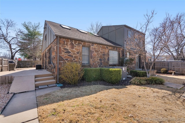 view of side of home with board and batten siding, fence, stone siding, and roof with shingles