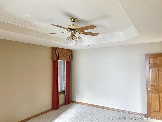 spare room with visible vents, baseboards, ceiling fan, light colored carpet, and a tray ceiling