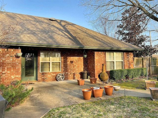 back of property featuring a patio, fence, brick siding, and roof with shingles