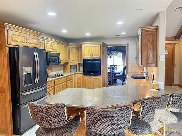 kitchen featuring light tile patterned floors, a peninsula, a sink, black appliances, and backsplash