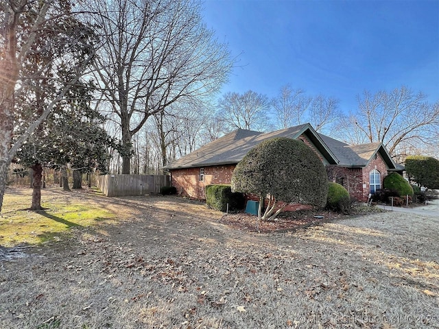 view of side of property with brick siding, driveway, and fence