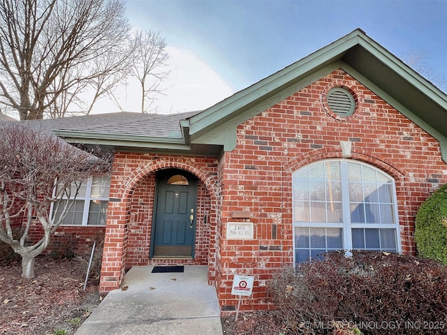 entrance to property featuring brick siding and roof with shingles