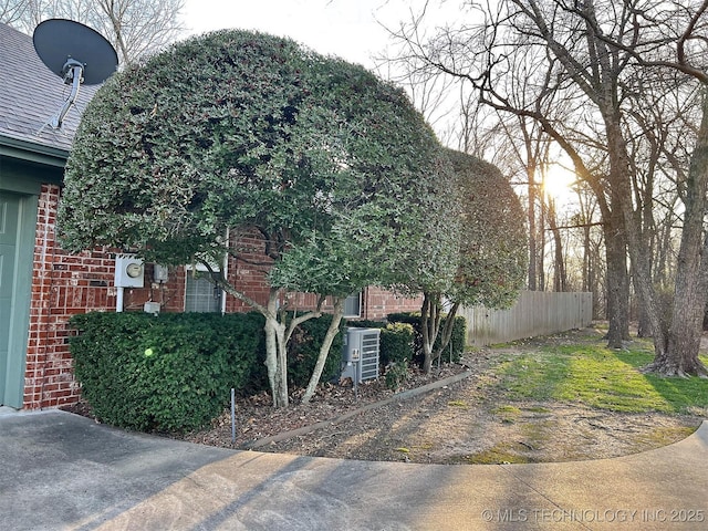 view of side of home featuring fence, brick siding, and a shingled roof