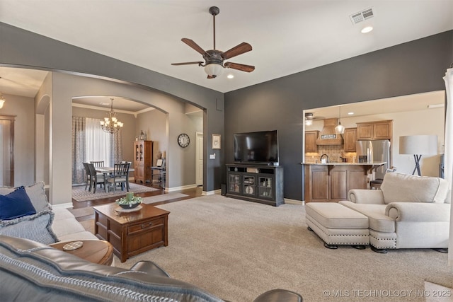 living area featuring visible vents, baseboards, arched walkways, ceiling fan with notable chandelier, and light colored carpet