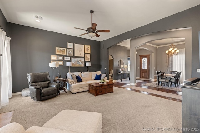 carpeted living area with visible vents, baseboards, vaulted ceiling, ceiling fan with notable chandelier, and arched walkways