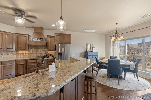 kitchen featuring backsplash, dark wood finished floors, a breakfast bar area, stainless steel refrigerator with ice dispenser, and custom exhaust hood