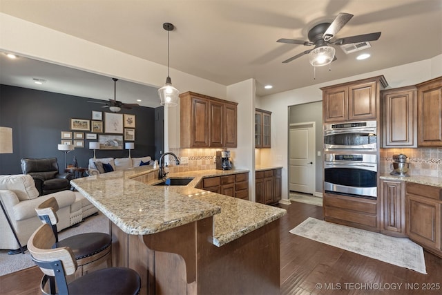 kitchen with dark wood-type flooring, a breakfast bar, a sink, double oven, and a peninsula