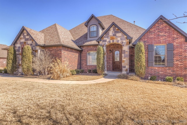 english style home with stone siding, brick siding, roof with shingles, and a front yard