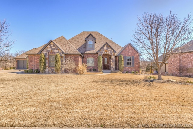 view of front of property with brick siding, stone siding, a front yard, and roof with shingles