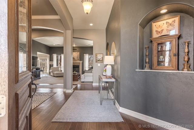 foyer entrance featuring a fireplace, wood finished floors, baseboards, and arched walkways