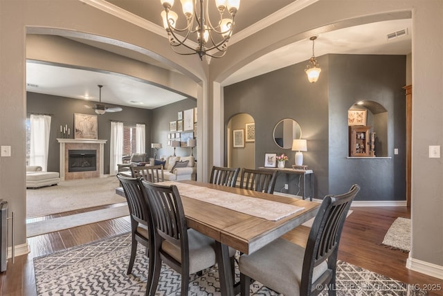 dining room featuring visible vents, baseboards, dark wood finished floors, arched walkways, and a tiled fireplace